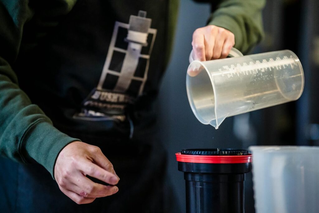 Hands pouring liquid from a measuring cup into a container, possibly for photo development.